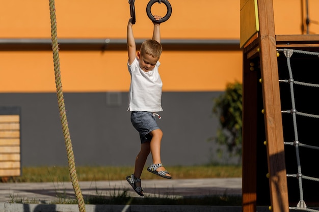 Il ragazzo con una maglietta bianca e pantaloncini nel parco giochi si arrampica sui giochi della parete da arrampicata per strada