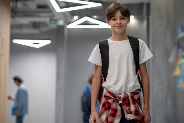 Мальчик в белой футболке с рюкзаком в школьном коридоре