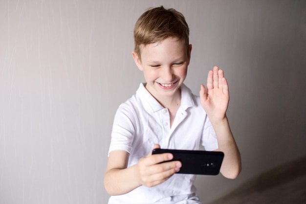 A boy in a white Tshirt with a black phone communicates via video chat