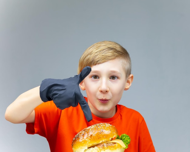 The boy who is sitting in front of the burger points at him with a finger on his hand he is wearing a black disposable glove
