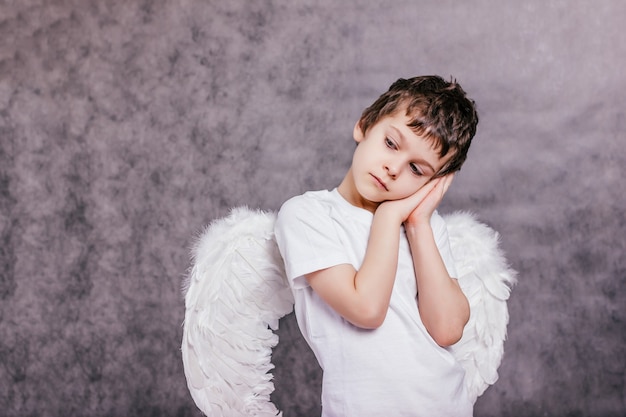 The boy with the angel wings on is tired and asleep on gray background copy space