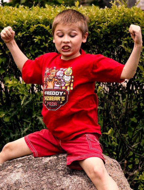 写真 腕を上げて岩の上に座っている少年