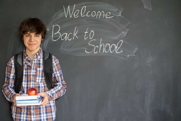 Boy with backpack, books and apple with back to school on black board