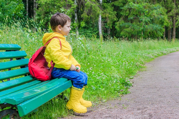 A boy with a backpack is sitting on a bench.