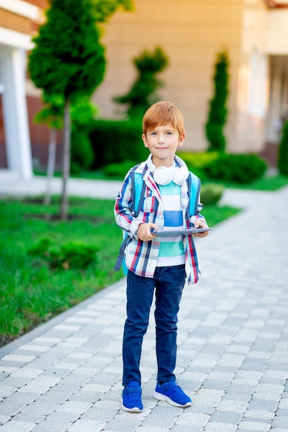 A boy with a backpack and a tablet with headphones at school reading a book or doing homework the concept is back to school