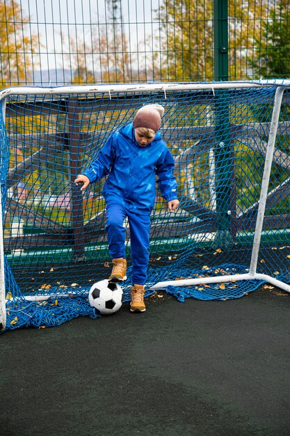 サッカーのゴールの近くにボールを持つ少年。アウトドアスポーツのコンセプト