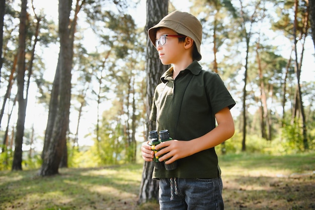 双眼鏡を持つ少年 一緒に夏の昼間に緑の森で子供