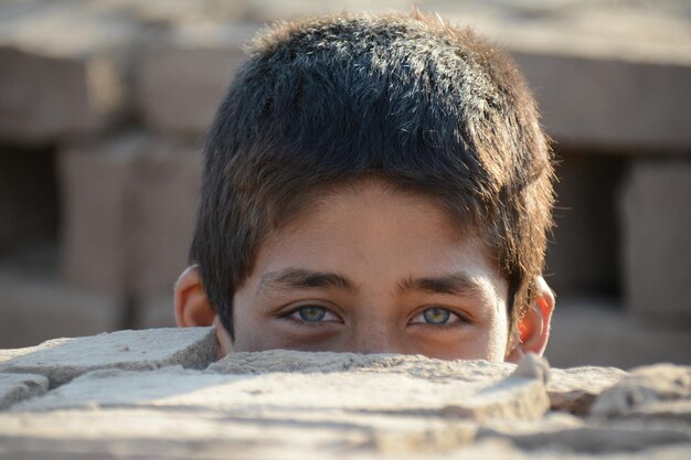 A boy with blue eyes looks over a hole in the ground.