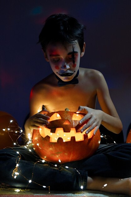 Photo boy with body paint holding illuminated jack o lantern