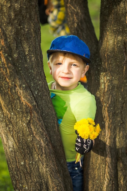 A boy with a bouquet of dandelions for mothers day among the trees in the park