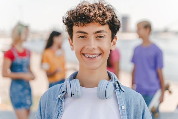 Foto ragazzo con le parentesi che indossa le cuffie guardando la telecamera in piedi per strada con gli amici