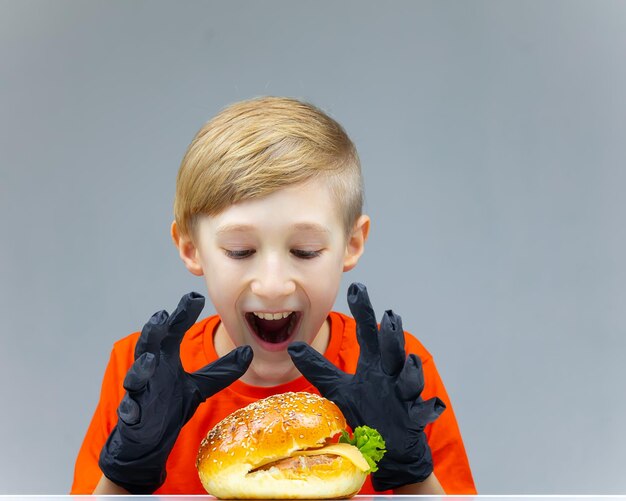 A boy with a cheeseburger at the table happily wants to grab it and sit down