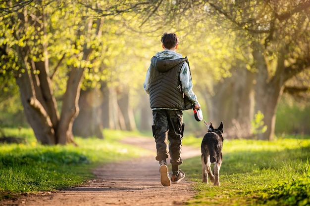 A boy with a dog walk in the park on a sunny spring evening run along the road Friendship of man and animal healthy lifestyle