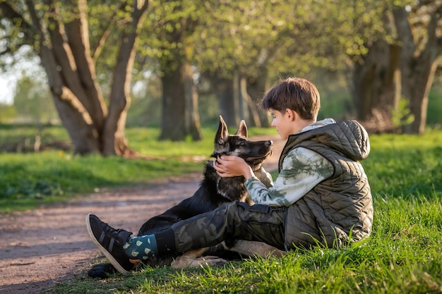 晴れた春の夜に公園を散歩する犬のいる少年が草の上に座る人と動物の健康的なライフスタイルの友情