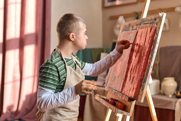 Photo boy with down syndrome painting on easel in art studio