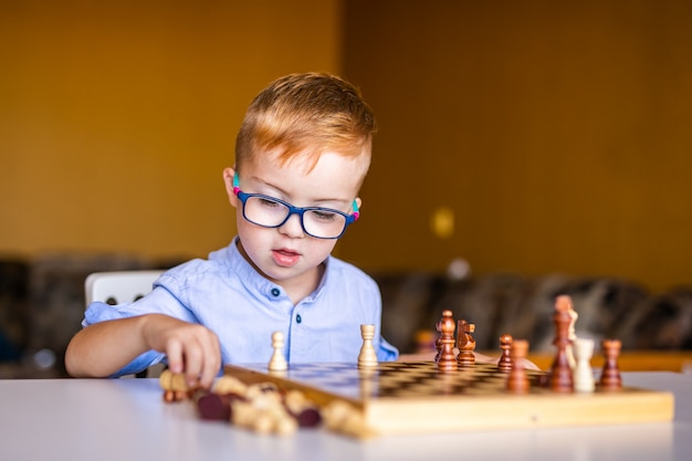 Boy with down syndrome with big glasses playing chess.