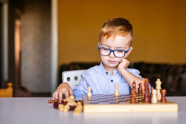 チェスをする大きな眼鏡のダウン症候群の少年