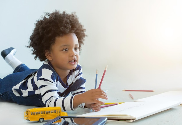 boy with drawing book and toy lying on white background