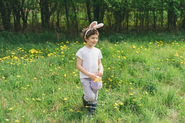 Boy with eggs basket and bunny ears on Easter egg hunt in sunny spring garden