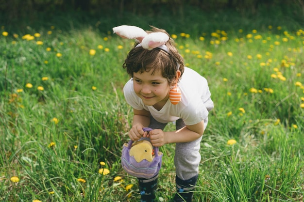 Boy with eggs basket and bunny ears on easter egg hunt in sunny spring garden