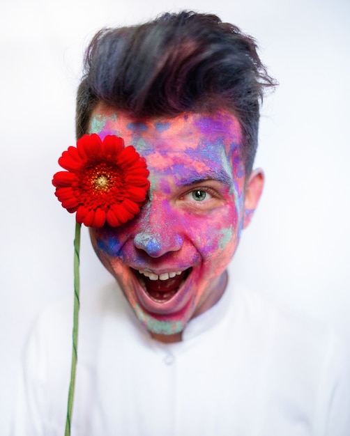 Boy with face covered with paints holds red flower before his eye