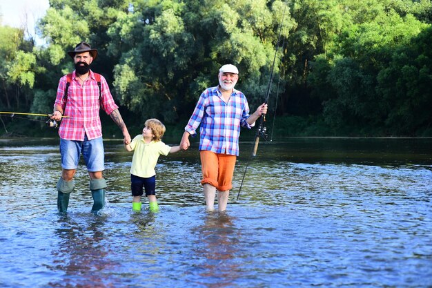 Boy with father and grandfather fly fishing outdoor over river background Man in different ages Hobby and sport activity