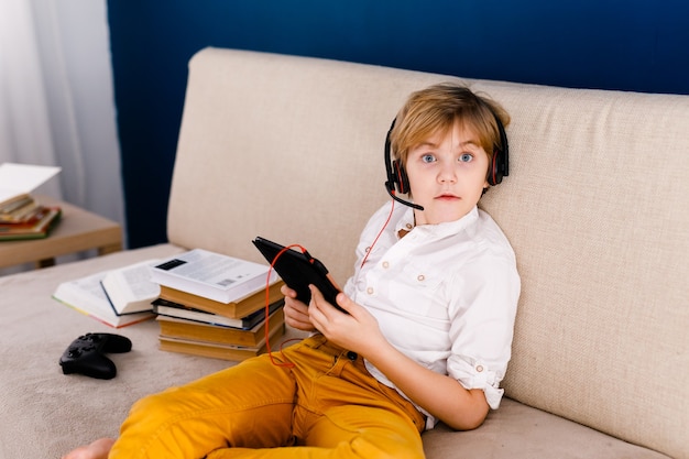 A boy with glasses and headphones is learning lessons with a tablet and books