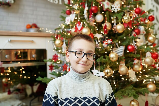 Boy with glasses sitting near Christmas tree