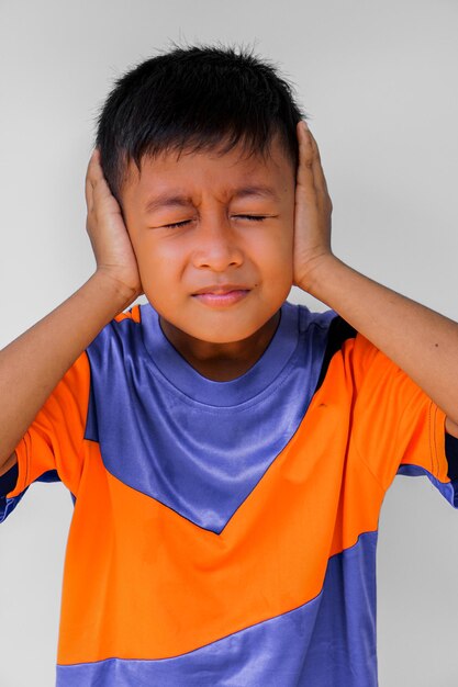 Boy with hands covering ears standing against wall