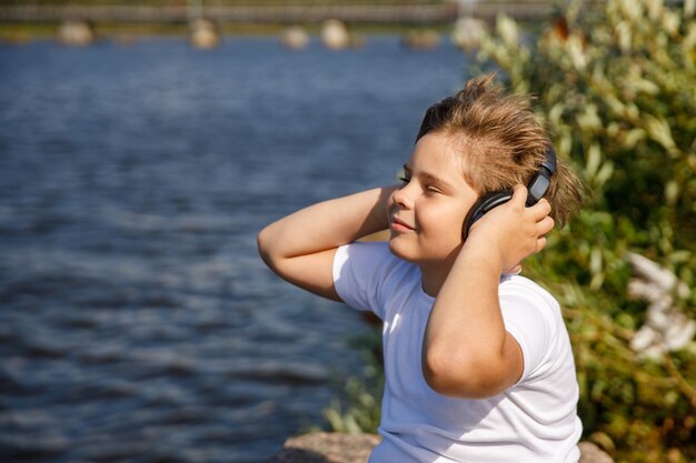 Boy with headphones listening to music by the lake