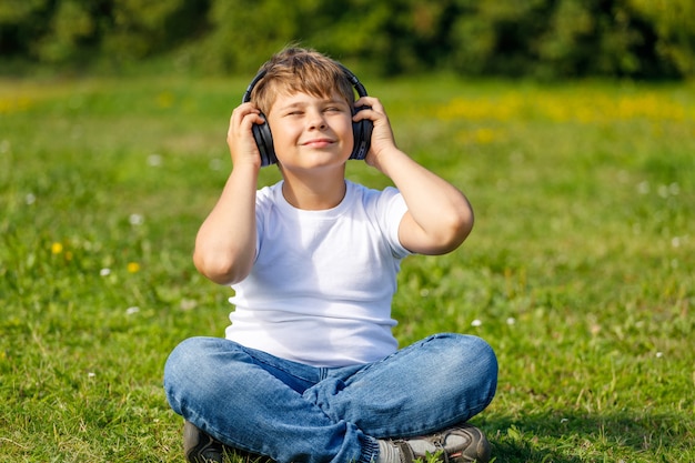 Мальчик в наушниках слушает музыку, сидя на траве