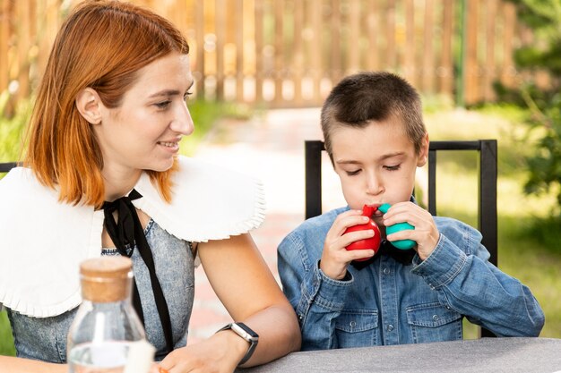 暖かい夏の日、庭で母親と一緒に男の子が2つのカラフルな風船を膨らませます。誕生日の準備