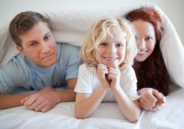 Boy with his parents under bed cover