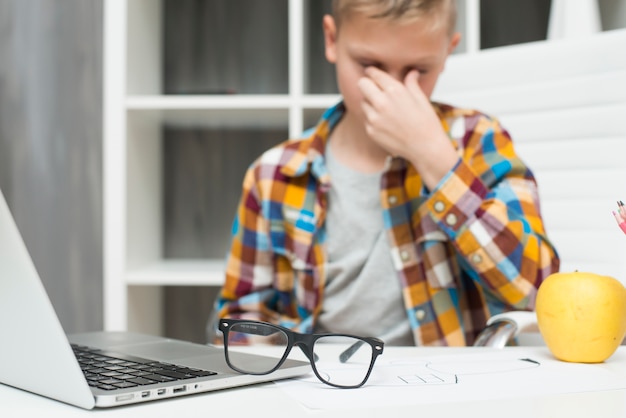 Foto ragazzo con il computer portatile allo scrittorio e l'espressione stanca