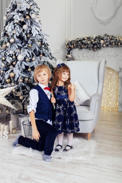 Boy with a little girl posing near the Christmas tree. 