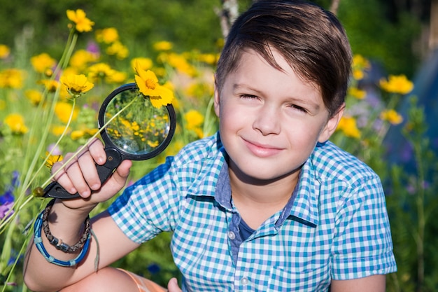 Boy with magnifying glass in summer garden