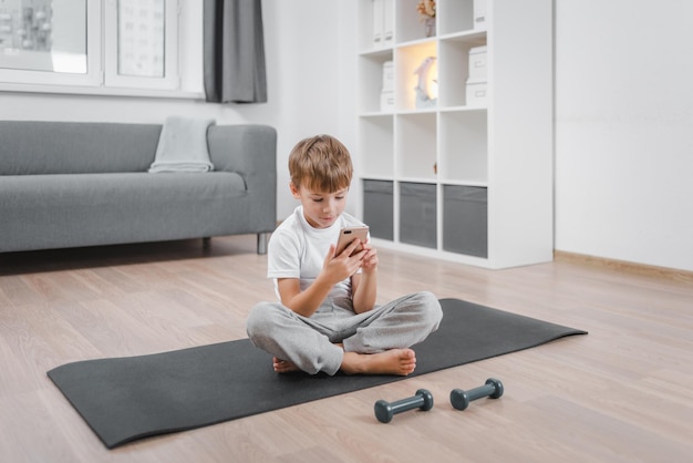 Boy with mobile phone after training with dumbbells. Studying online fitness lessons.