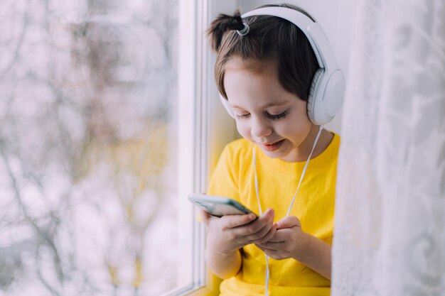 A boy with a phone is sitting on a lifestyle window . Social media. Modern children. An article about developed children.