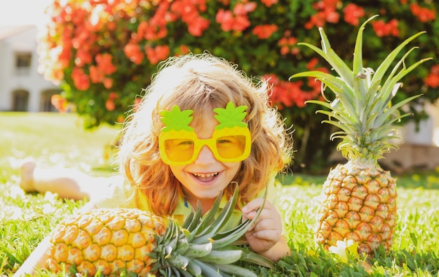 Boy with pineapple on head plays with fresh tropical fruit outdoorst excited funny kid child face wi