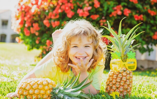 Boy with pineapple on head plays with fresh tropical fruit outdoorst excited funny kid child face wi