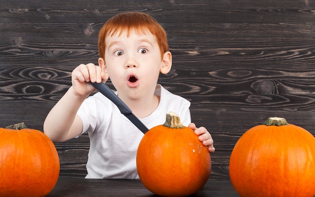 Un ragazzo con i capelli rossi tagliati con un coltello da zucca mentre prepara un pasto o per halloween