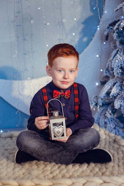 A boy with red hair and freckles on a blue background and a snow-covered tree