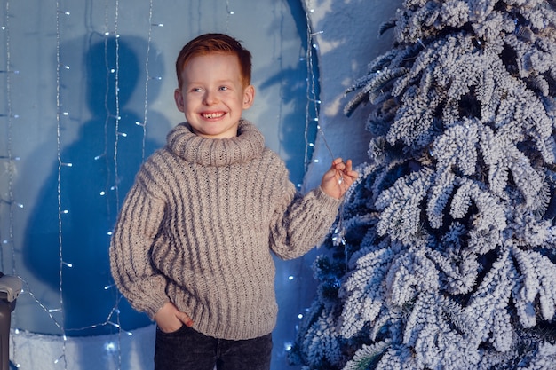 A boy with red hair and freckles next to christmas tree