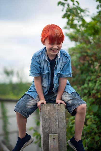 A boy with red hair is sitting on a wooden post