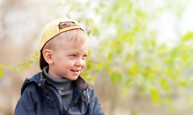 a boy with a smile is looking away against the background of the fresh greenery of spring