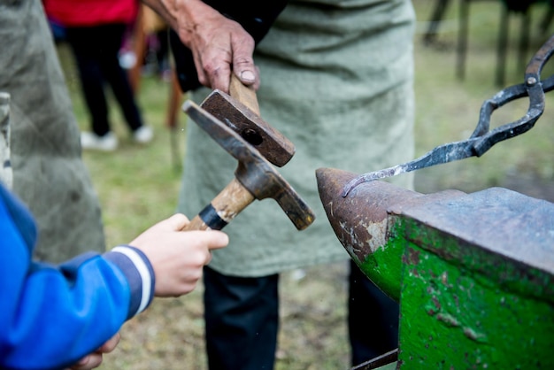 Boy with teacher forges detail. Education boy outdoors. Blacksmith craft. Smith teaches a child.