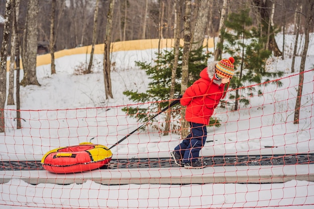 Boy with tubing rises on a travelator to the mountain Child having fun on snow tube Boy is riding a tubing Winter fun for children