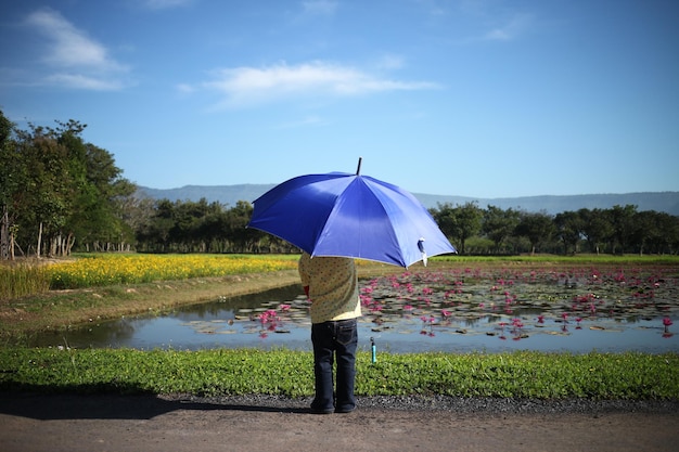写真 空に照らして湖のそばに立っている傘を持った少年