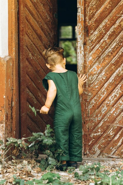 A boy with white hair in a green combination plays next to the wooden old door