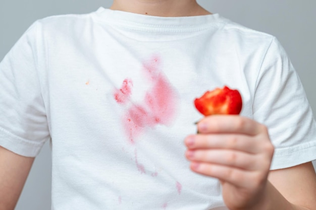 A boy with a white shirt that has a piece of strawberry